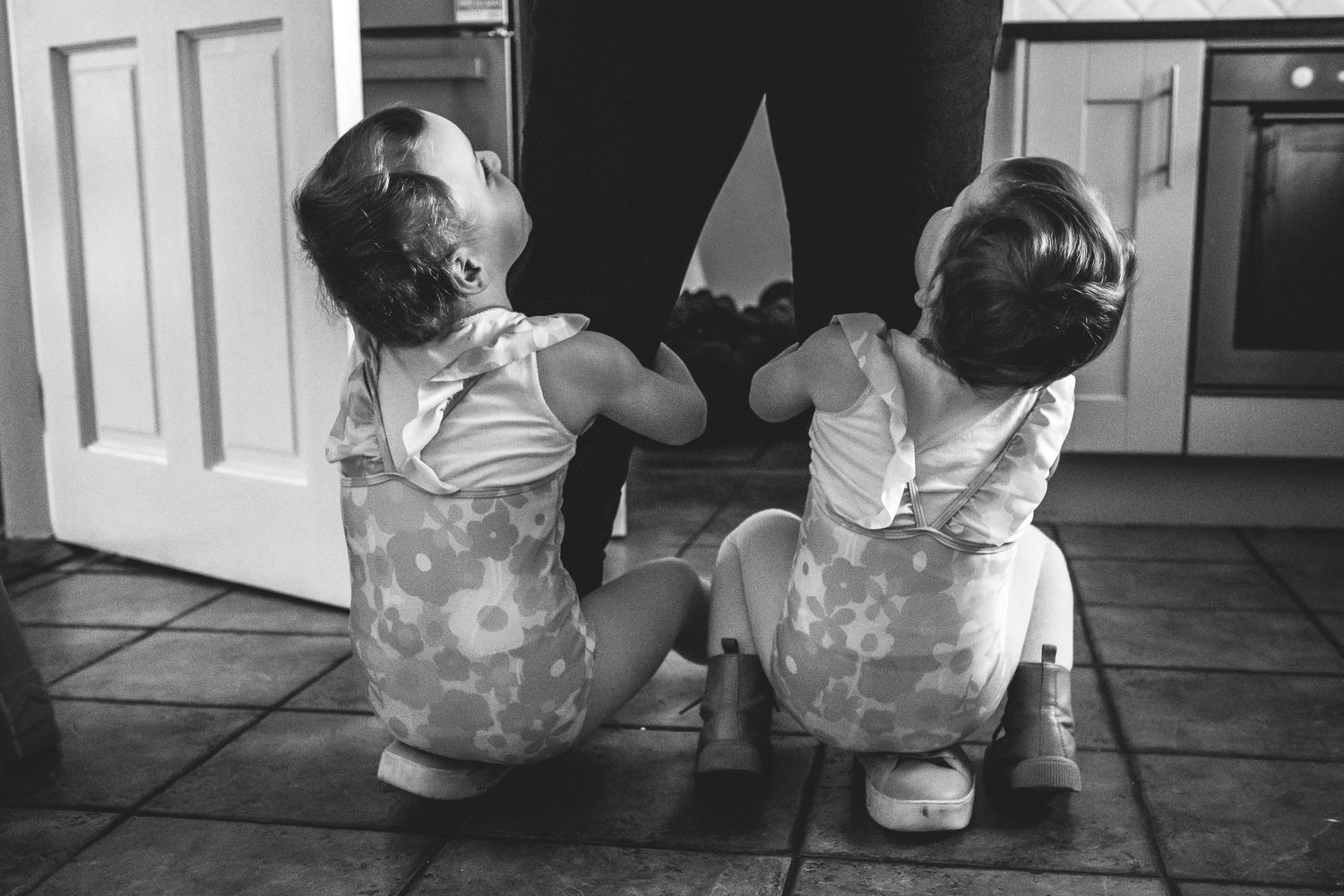 Black and white photo of two small figures in matching outfits playing on floor.