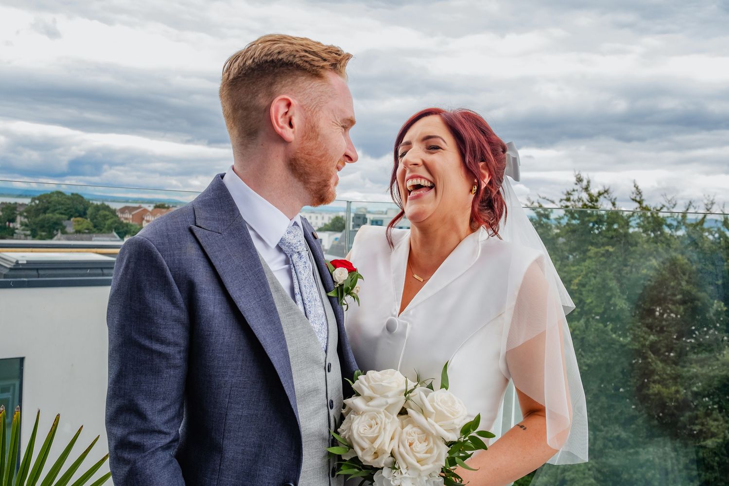A happy couple shares a joyful moment together on their wedding day, with the bride holding a white bouquet.