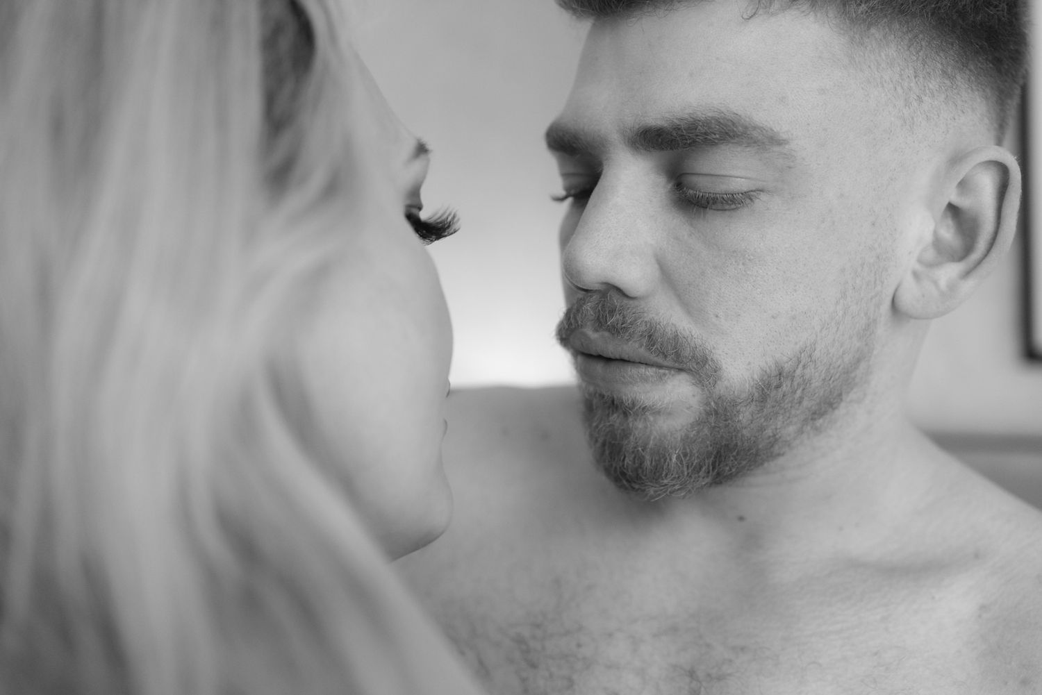 A close-up intimate black and white portrait of two people about to kiss, showing tenderness and connection.