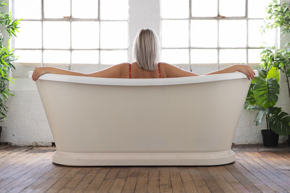 A blonde lady in a white freestanding bathtub posing for a boudoir photoshoot.