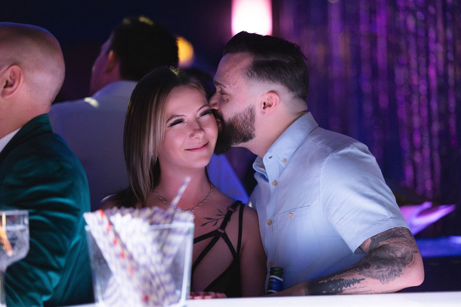 Couple sharing an intimate moment in dimly lit venue, purple lighting creating a romantic adult lifestyle event atmosphere