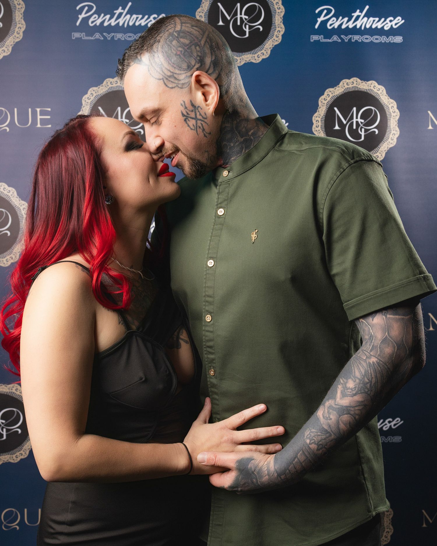 Couple posing intimately against branded event backdrop, showcasing adult lifestyle photography with stylish, confident energy