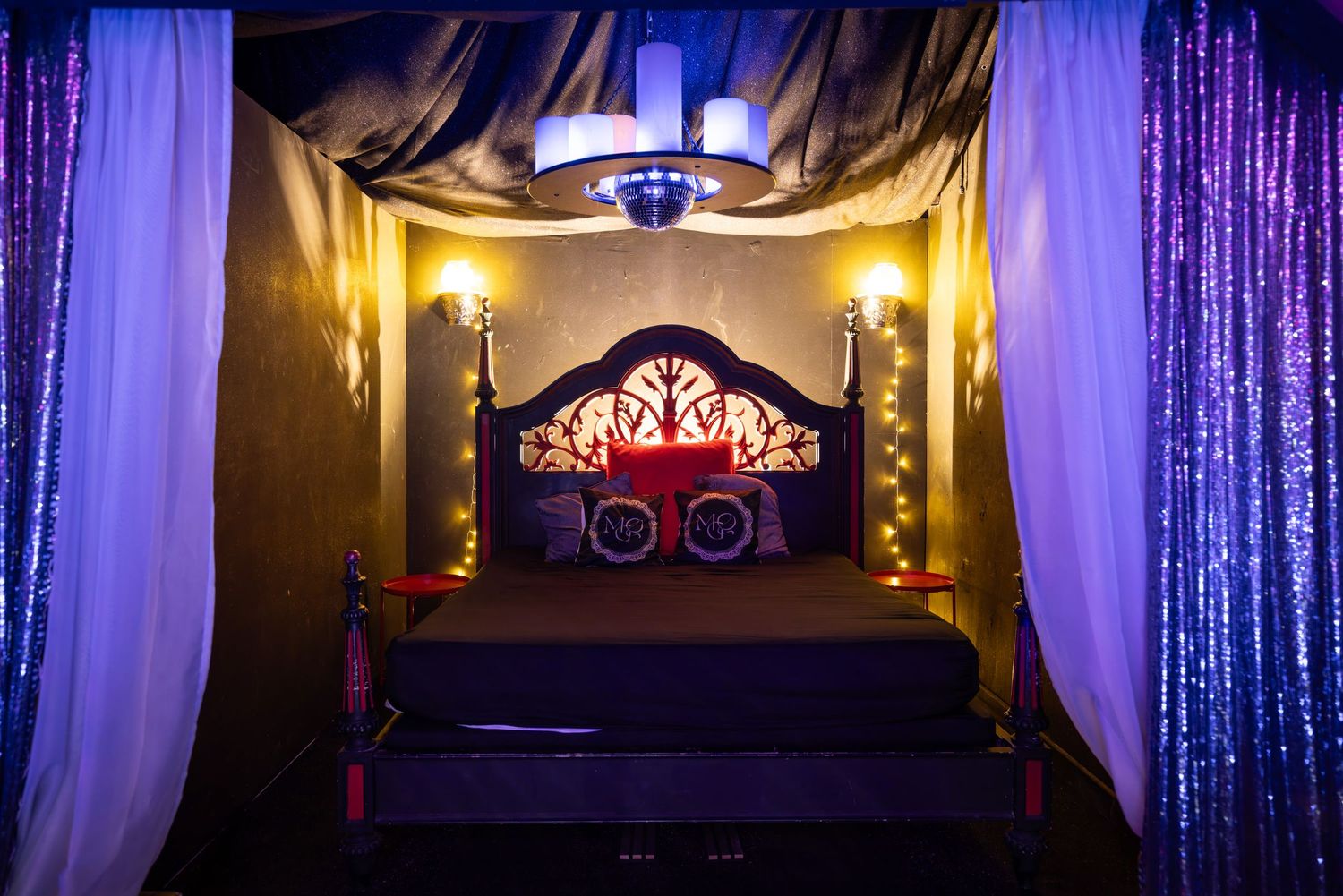 Ornate bed with purple uplighting and draped fabric at Penthouse Playrooms Dunstable, creating a sensual adult club interior setting