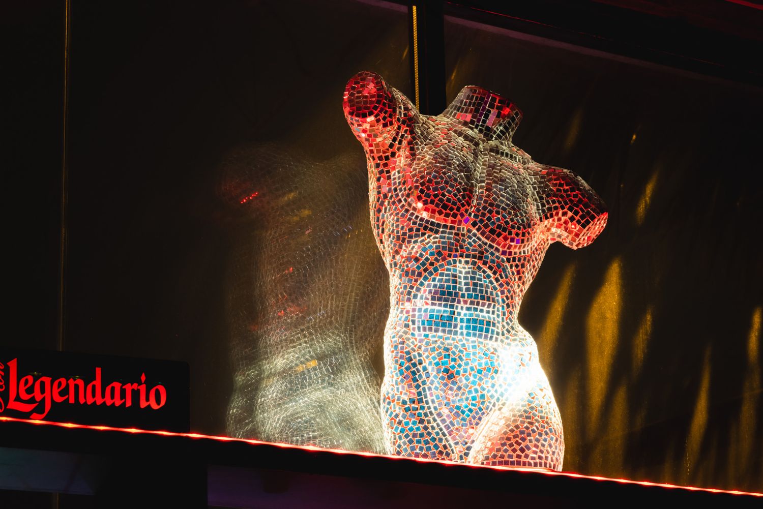 Illuminated crystalline sculpture of a torso shimmers with red and white lights against dark background.