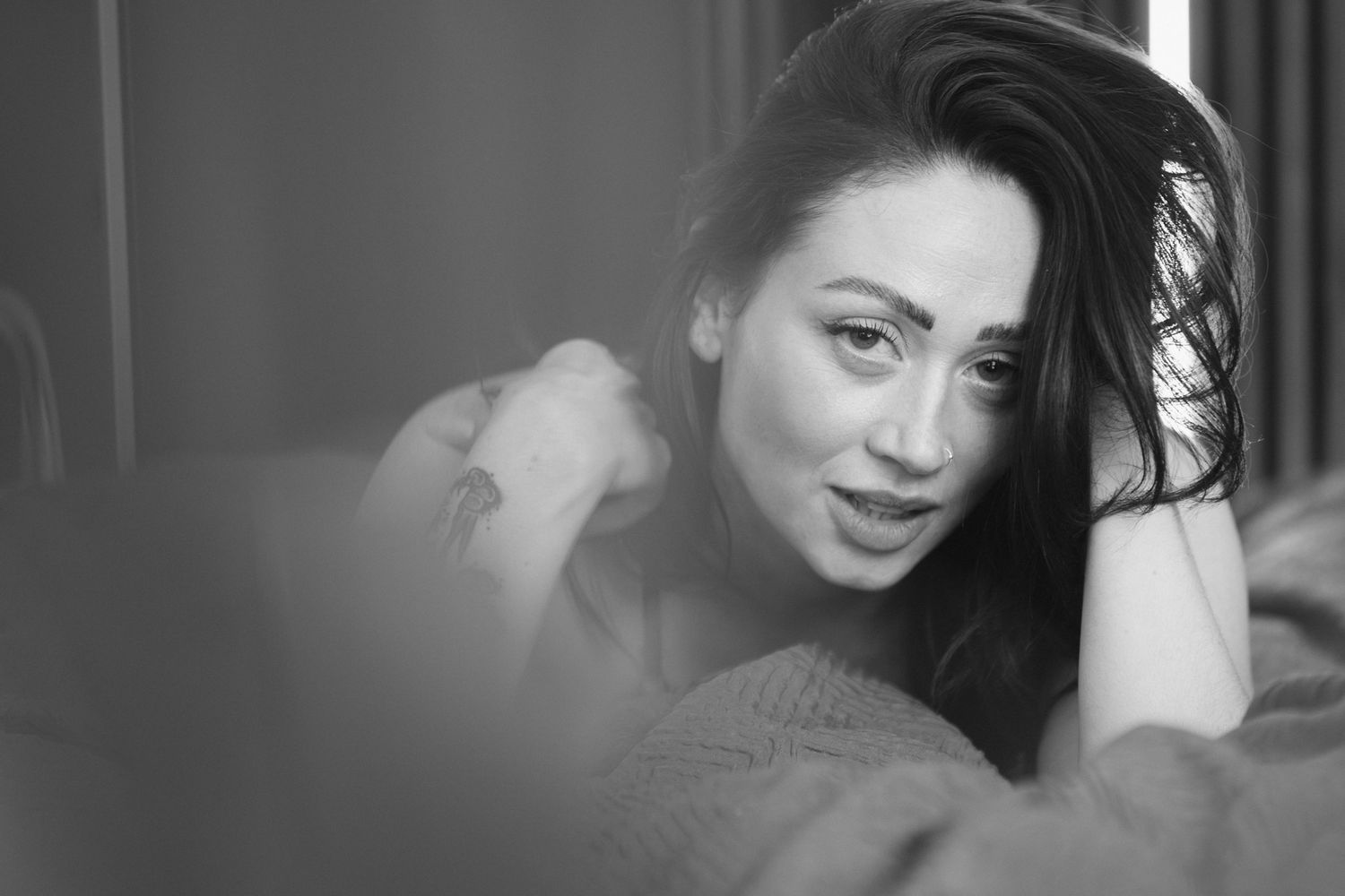 Black and white portrait of someone with long dark hair smiling while reclining in soft lighting.