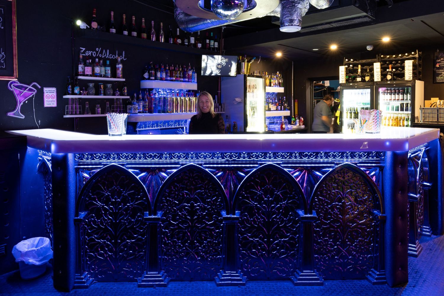 Modern bar with blue ambient lighting at Penthouse Playrooms Dunstable, illuminating bottles and glassware in a stylish adult club setting