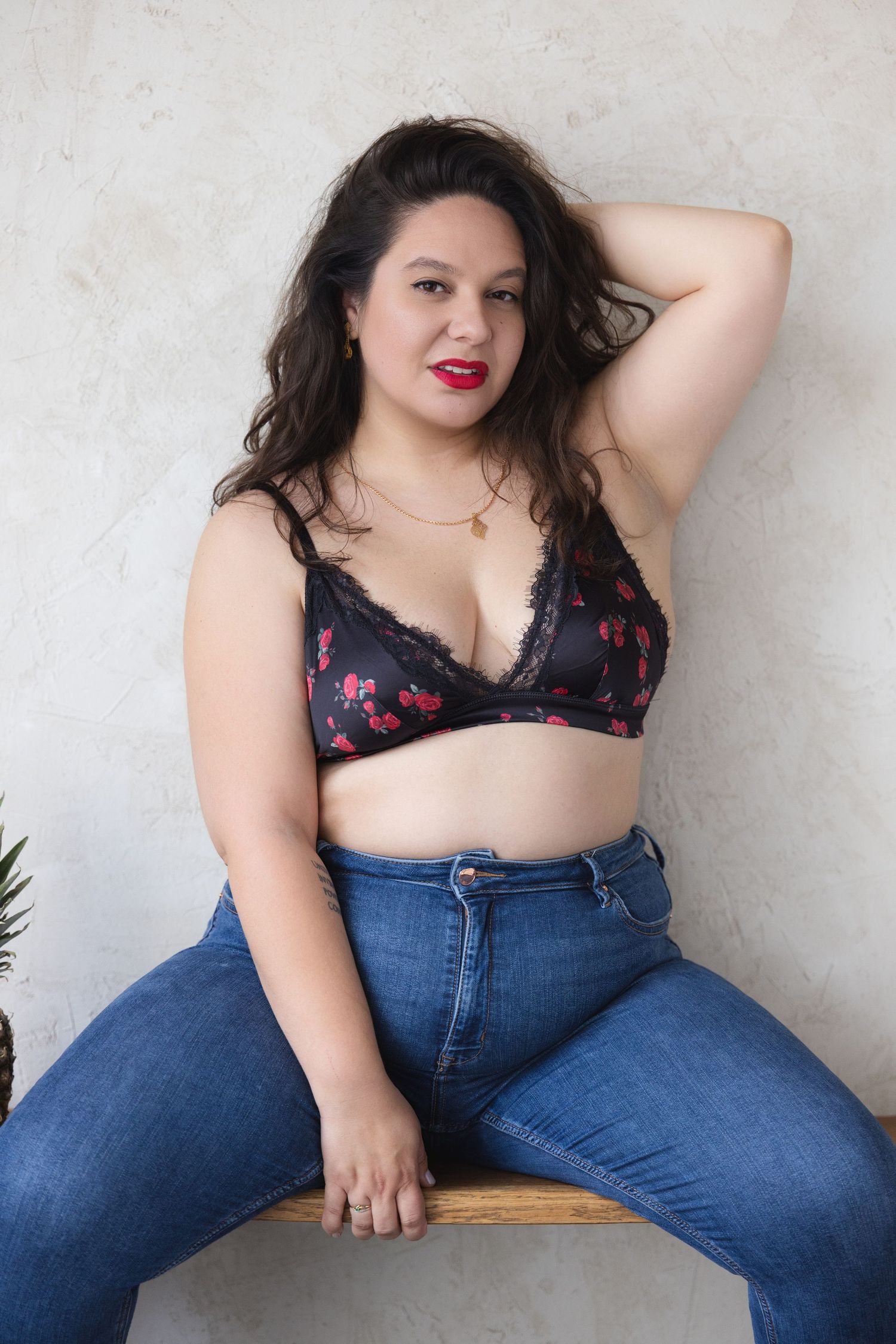 Plus-size woman in cherry print bralette and blue jeans posing confidently for a boudoir shoot in a Northampton studio.