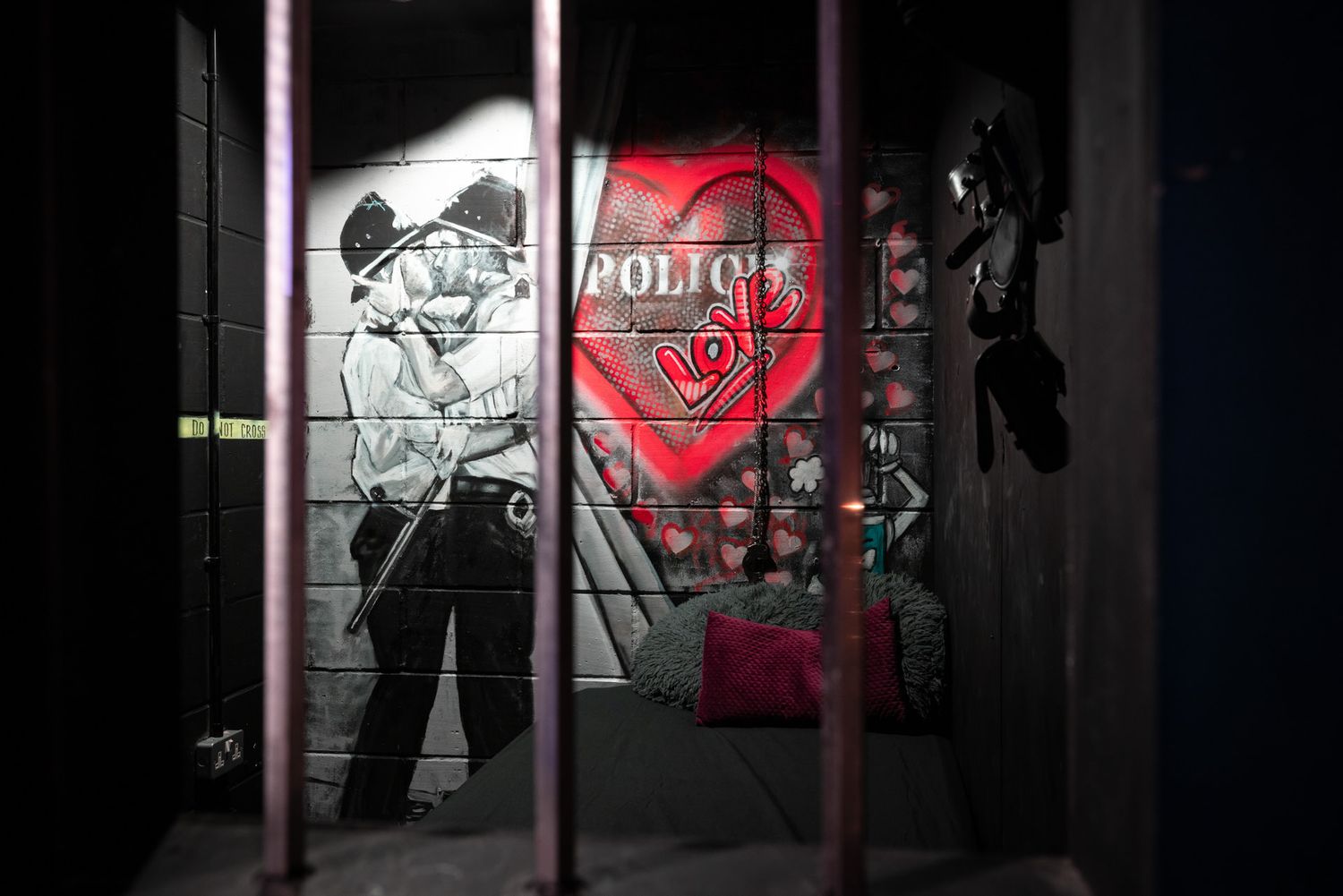 Street art mural through window bars shows black and white character figure next to red heart design in dark setting.