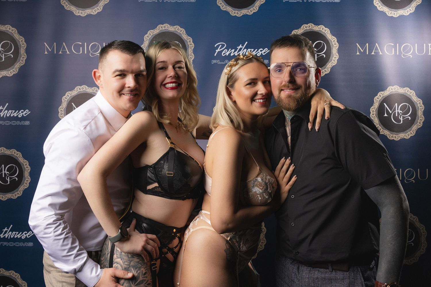 Group laughing and posing at adult lifestyle event, branded backdrop capturing social atmosphere and vibrant swingers party energy