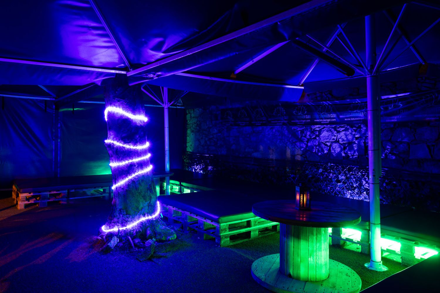 An industrial nightclub space illuminated with neon blue and green lights featuring glowing LED strips and exposed beams.