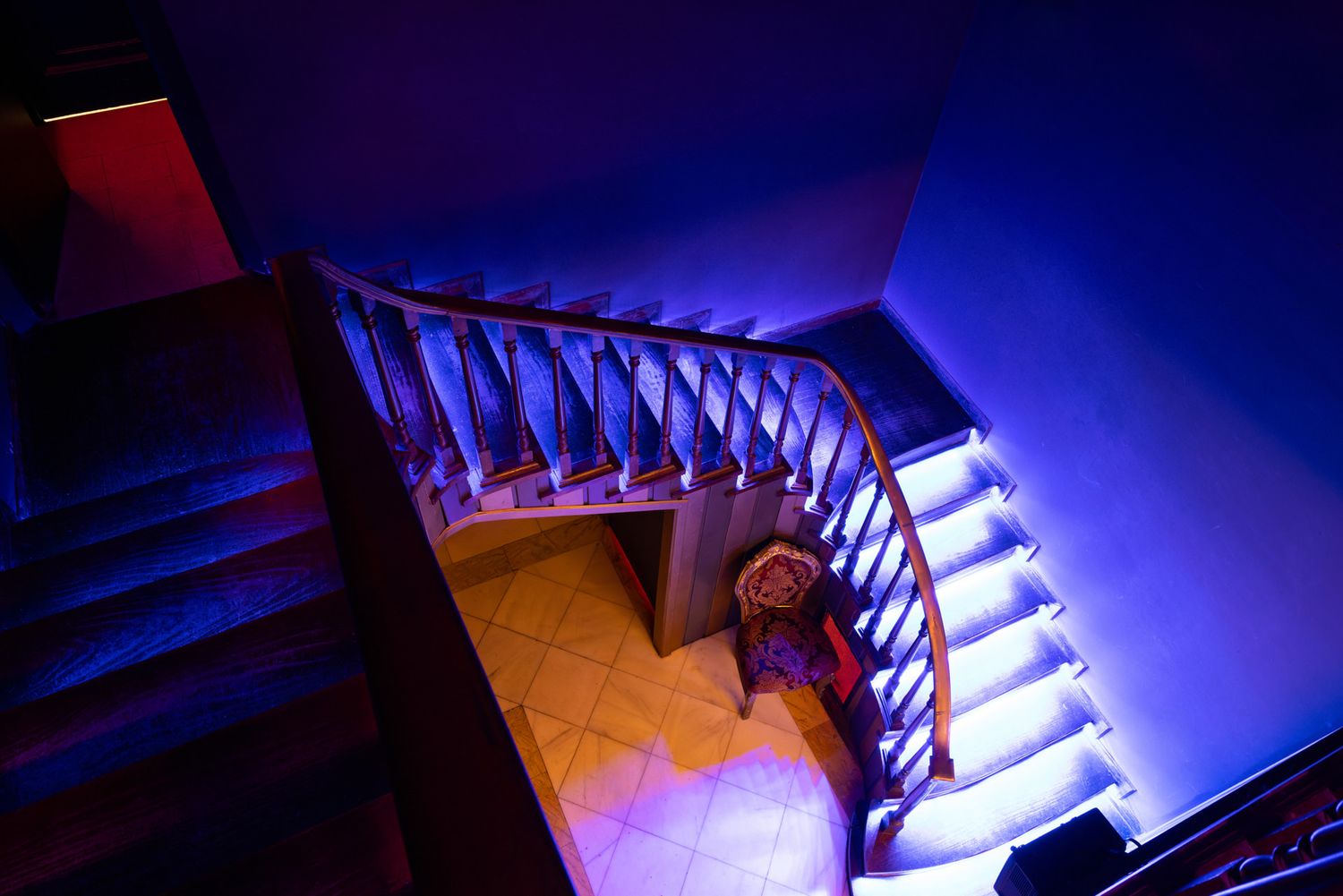Wooden staircase illuminated by dramatic blue lighting creates an atmospheric scene with curved bannister and wooden steps.