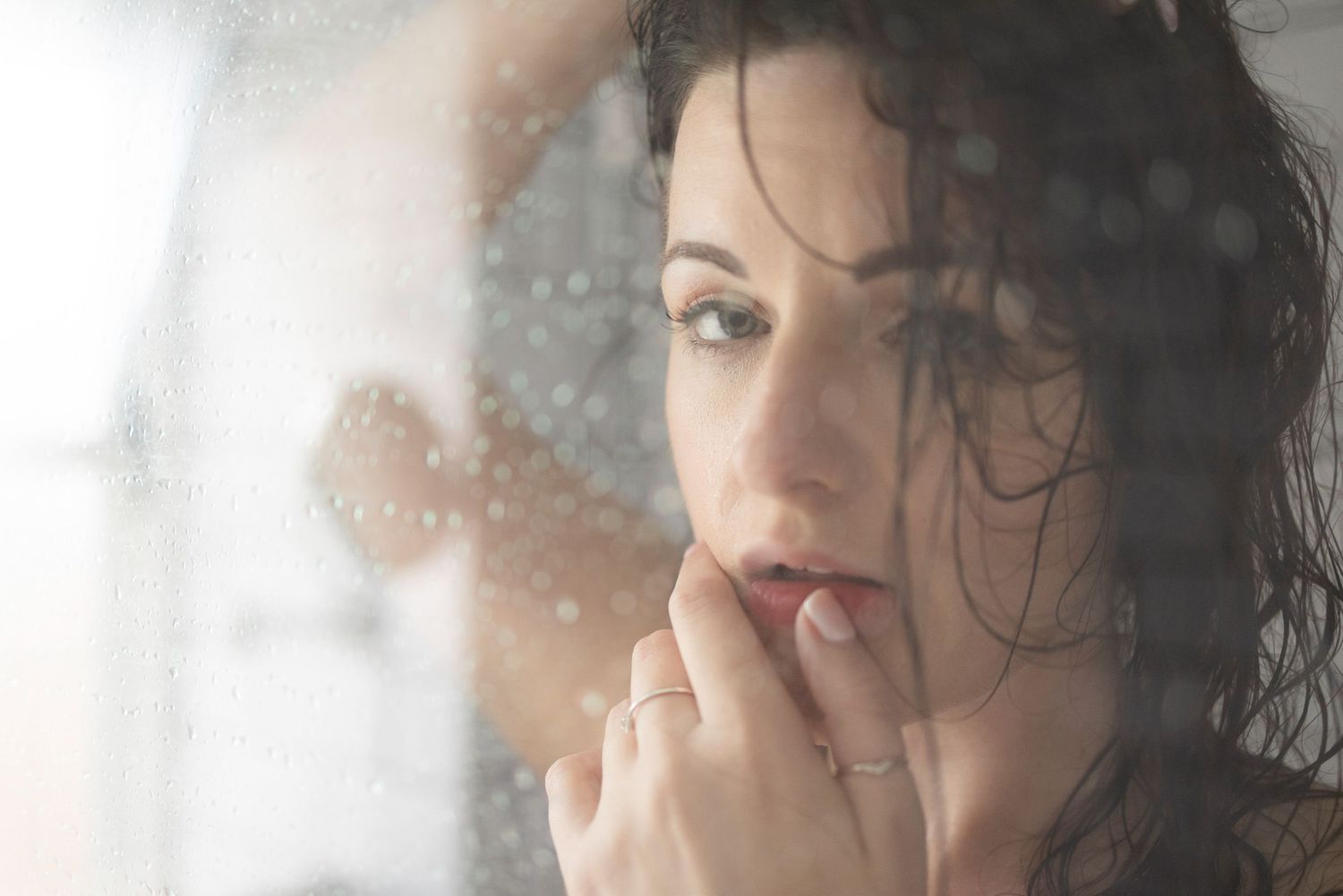 Woman with wet hair behind misted glass touching lips - moody intimate boudoir photography portrait with soft light