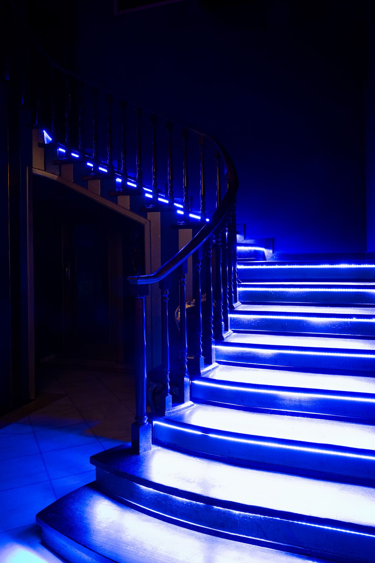 A curved staircase illuminated with blue LED lights along the steps and handrail creates a dramatic nighttime atmosphere.