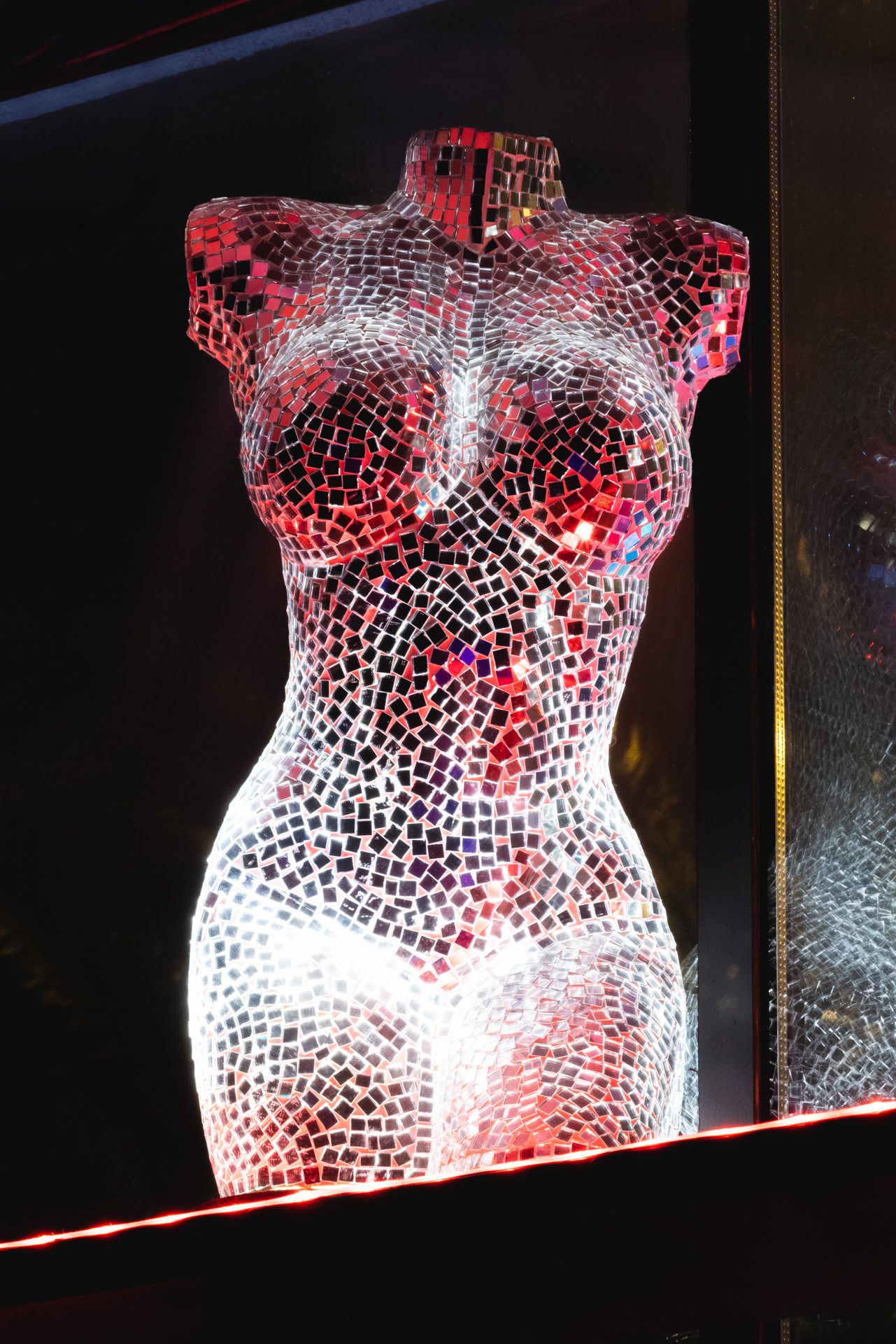 Abstract white mesh torso sculpture with red illumination creates a striking modern art display in a dark gallery space.