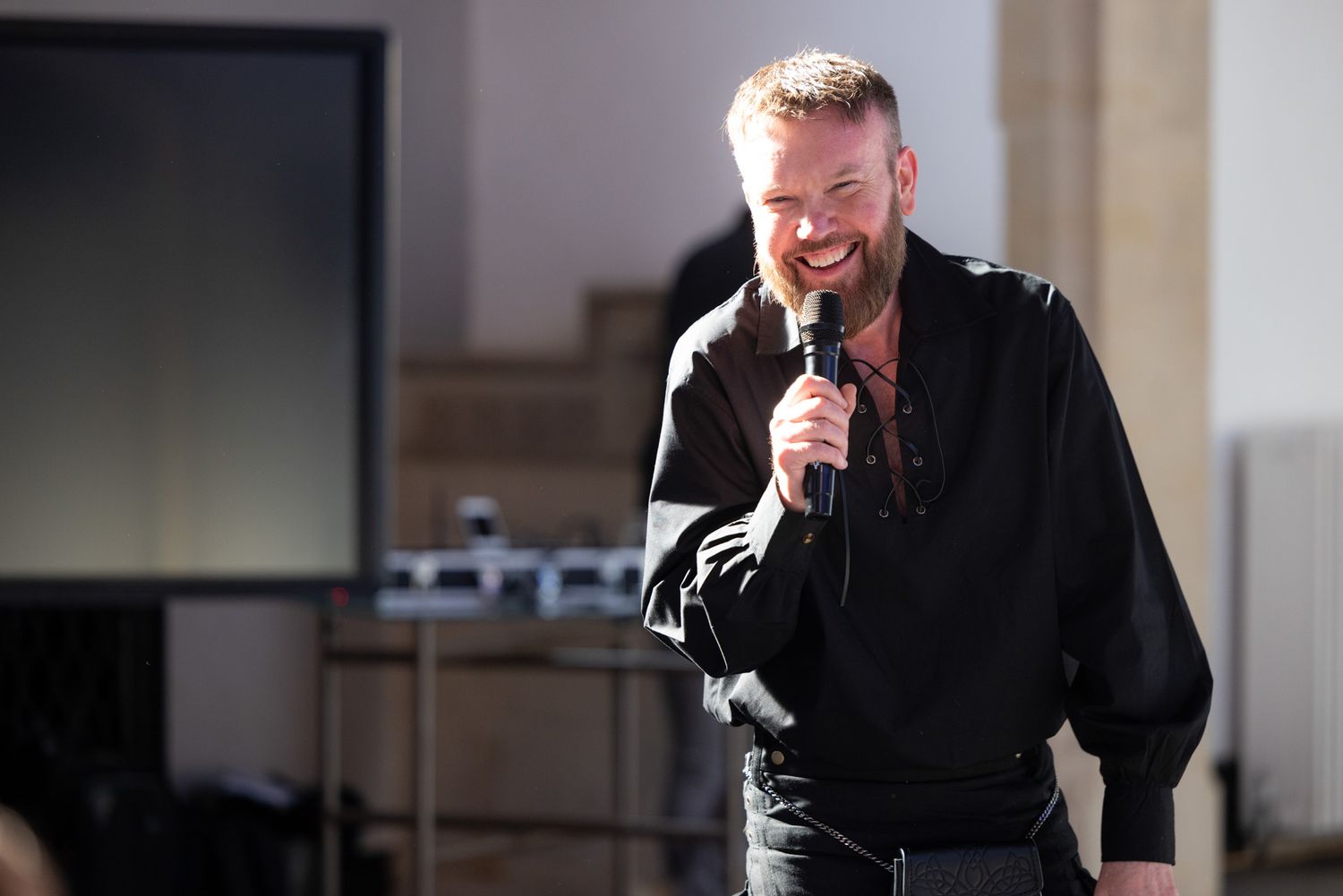 A performer in a black shirt holds a microphone and smiles while singing on stage.