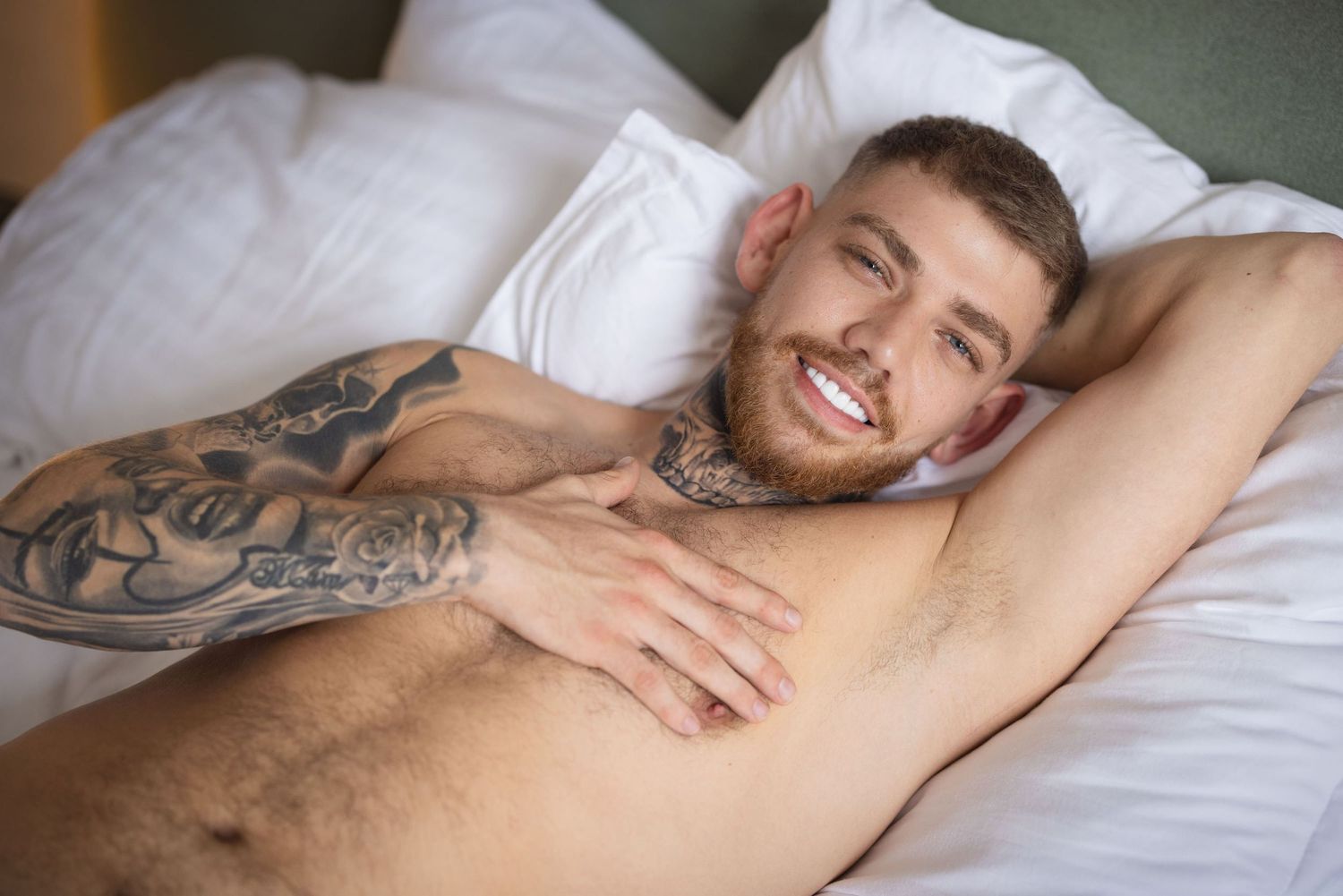 Person lying on white bedding with visible tattoos on arm and torso.