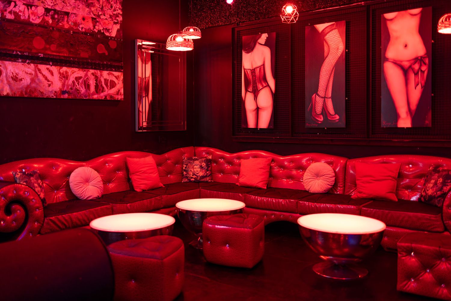 Dark red-lit interior of an adult entertainment venue with neon lights and lounge seating.