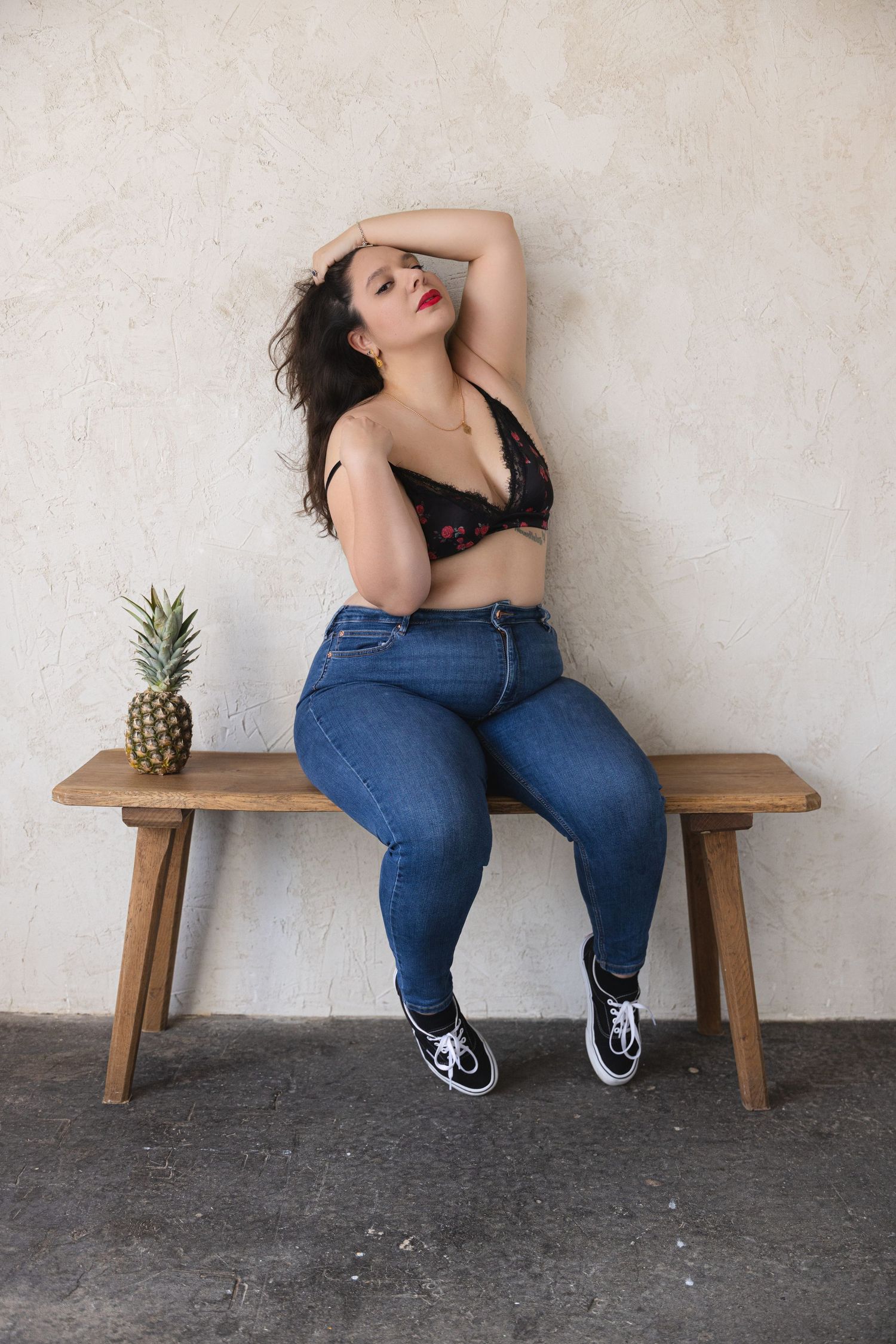 Plus-size woman in black lace bralette and blue jeans posing for a boudoir shoot on a wooden bench in a Northampton studio.