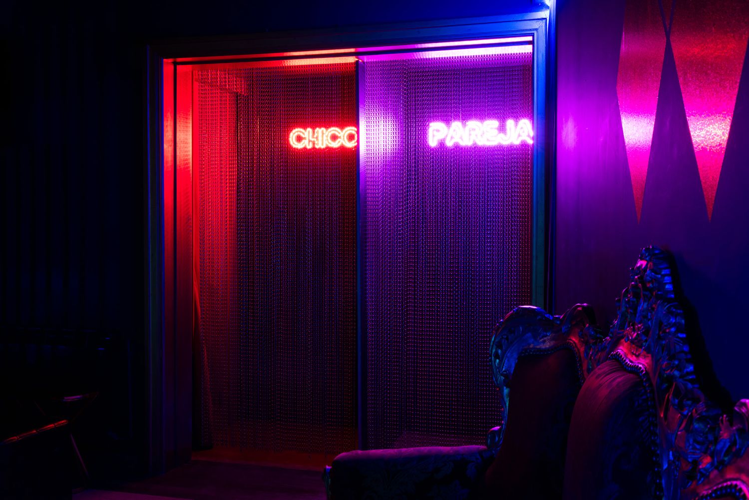 Neon sign glowing in red and purple lights against a dark wall with ambient lighting creating a moody atmosphere.