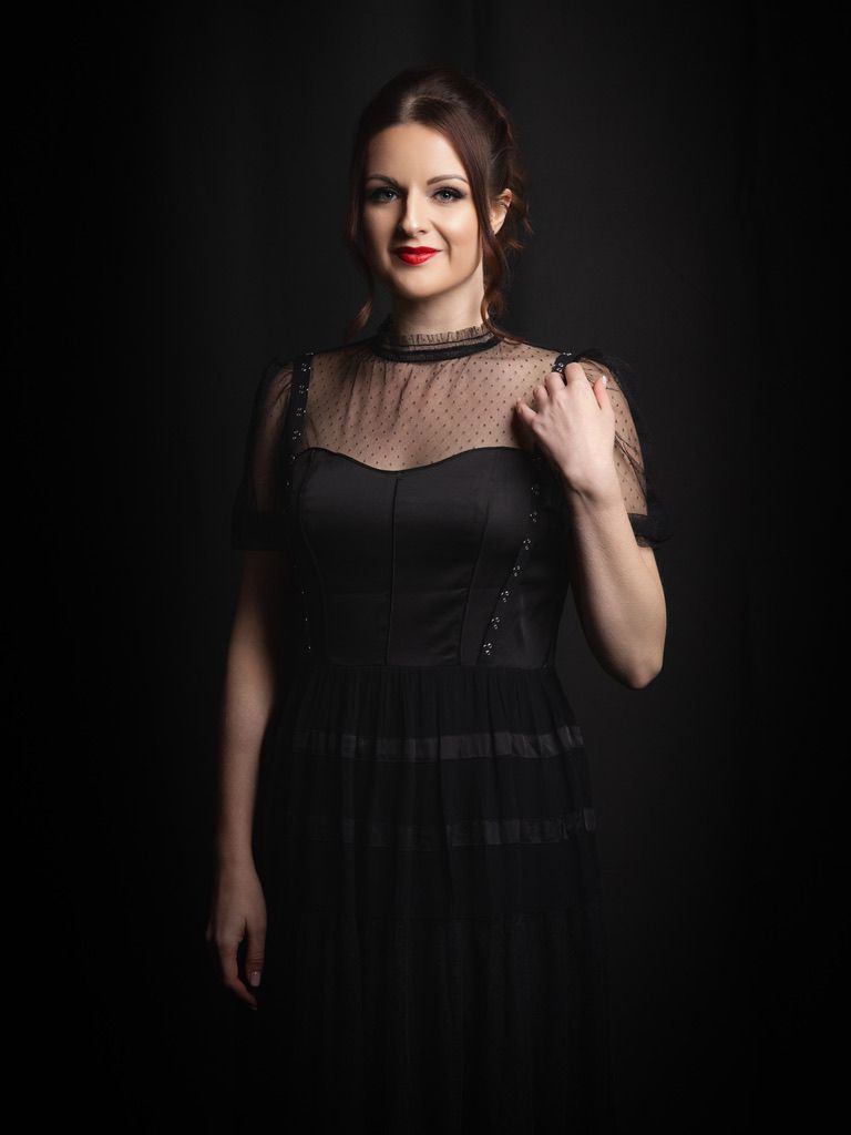 Woman in elegant black evening wear with sheer details and red lipstick - dramatic low-key boudoir portrait against dark background