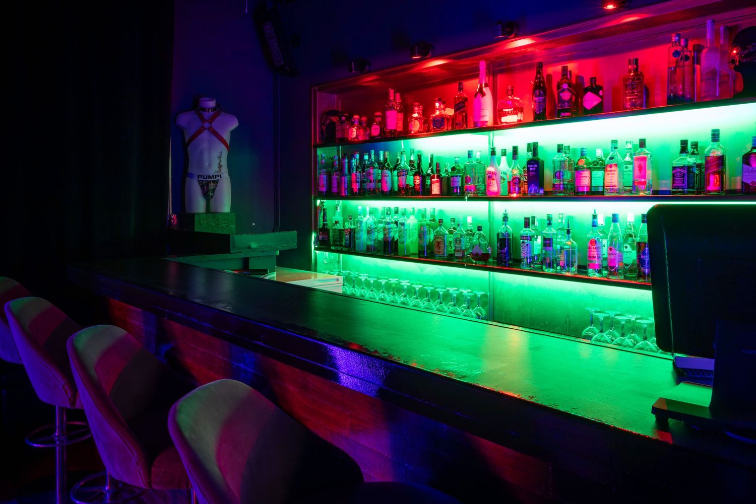 Neon-lit bar shelves with red to green lighting at Club Oops Barcelona, creating a vibrant nightclub interior atmosphere