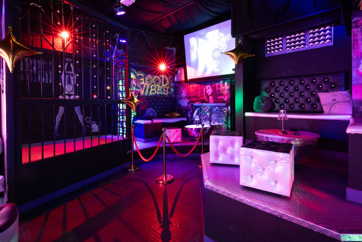 Purple and red neon lights illuminate a modern swingers club interior with multiple screens and sleek design elements.