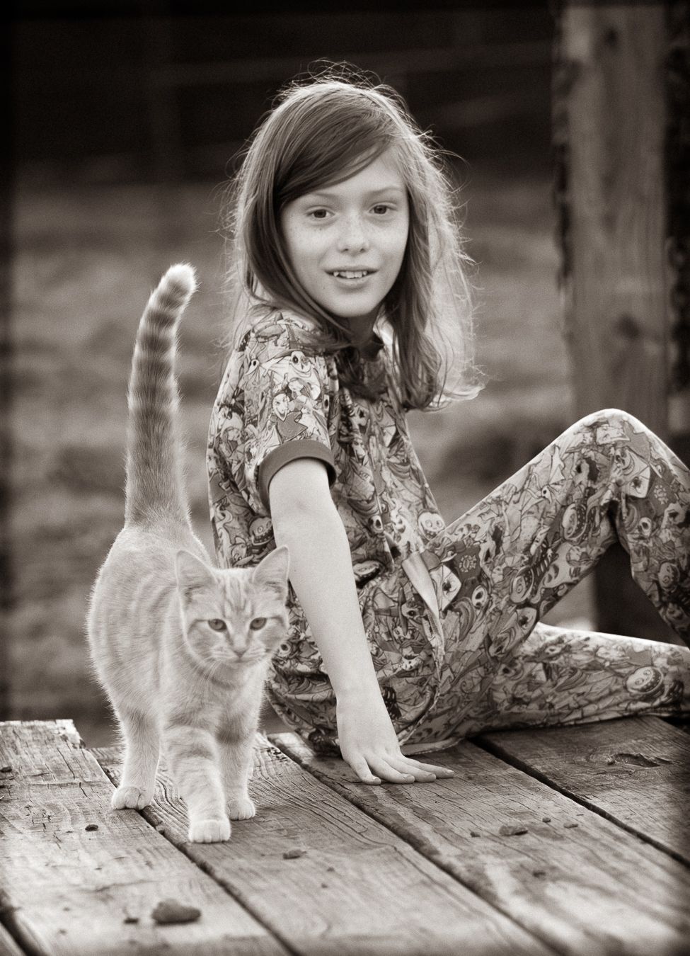 Black and white photo of a young boy sitting on a wooden deck petting an orange kitten.