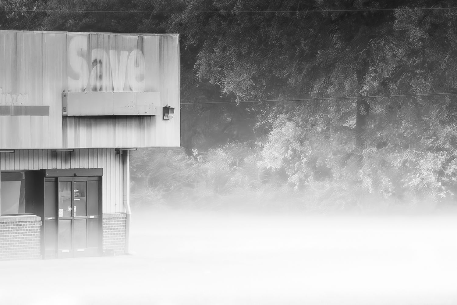 Black and white photo of a flooded building with a Store sign surrounded by misty fog and trees.