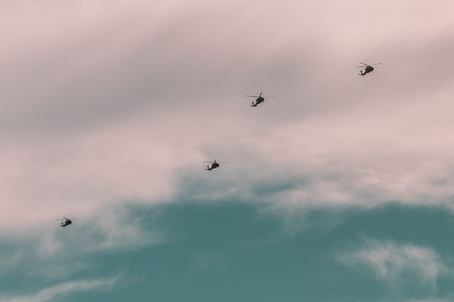 Five military helicopters flying in formation against a cloudy sky with soft pink and blue tones.