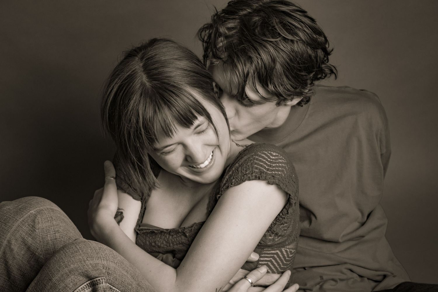 A couple shares a tender moment, with a man kissing a smiling woman on the cheek in a sepia-toned portrait.