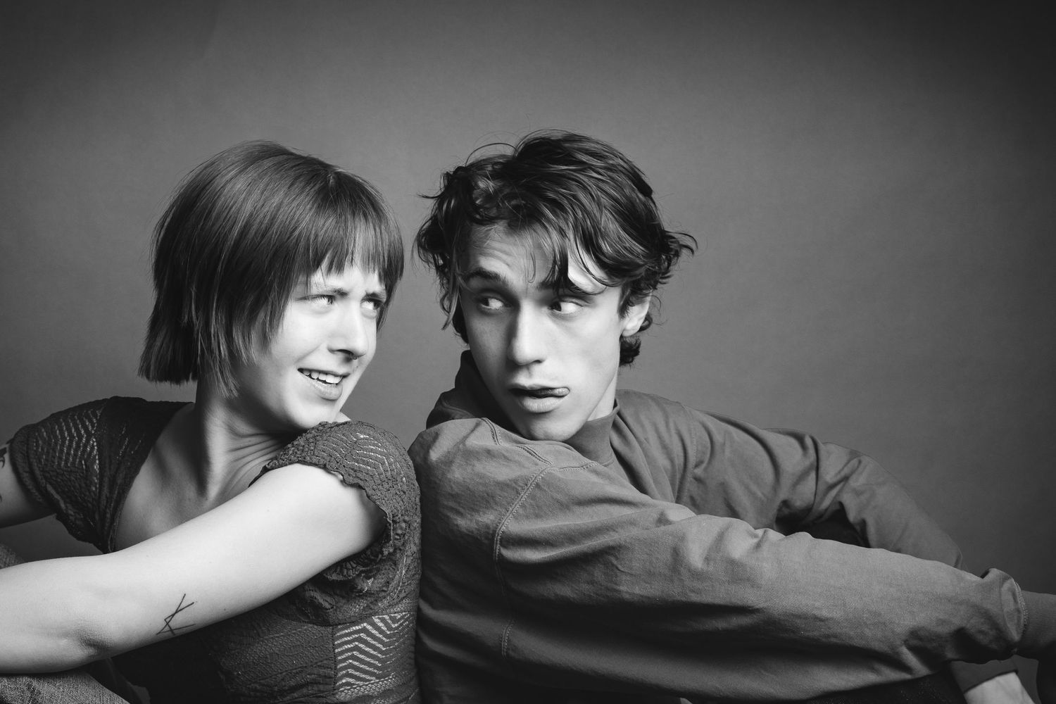 Black and white portrait of a young woman and man posing together against a gray studio background.