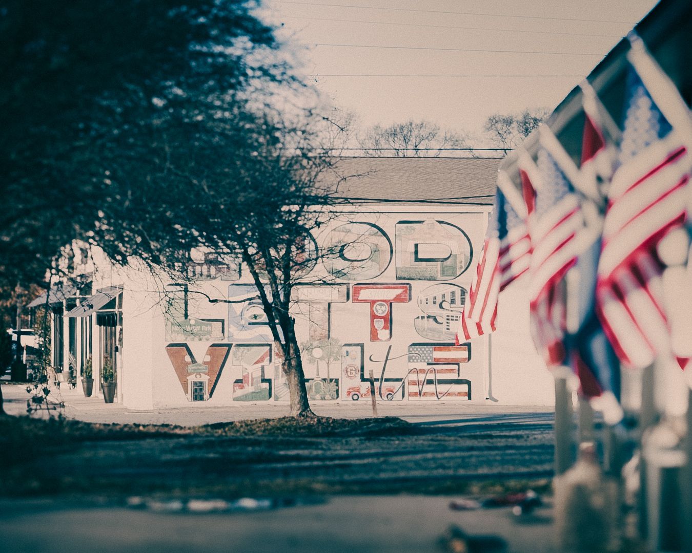 American flags line a street beside a building with large decorative GOODLETTSVILLE letters outdoors.