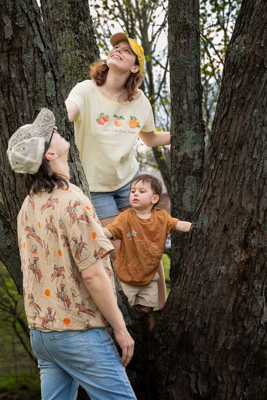 Family of three climbing large tree trunk together, mother and toddler perched between branches.