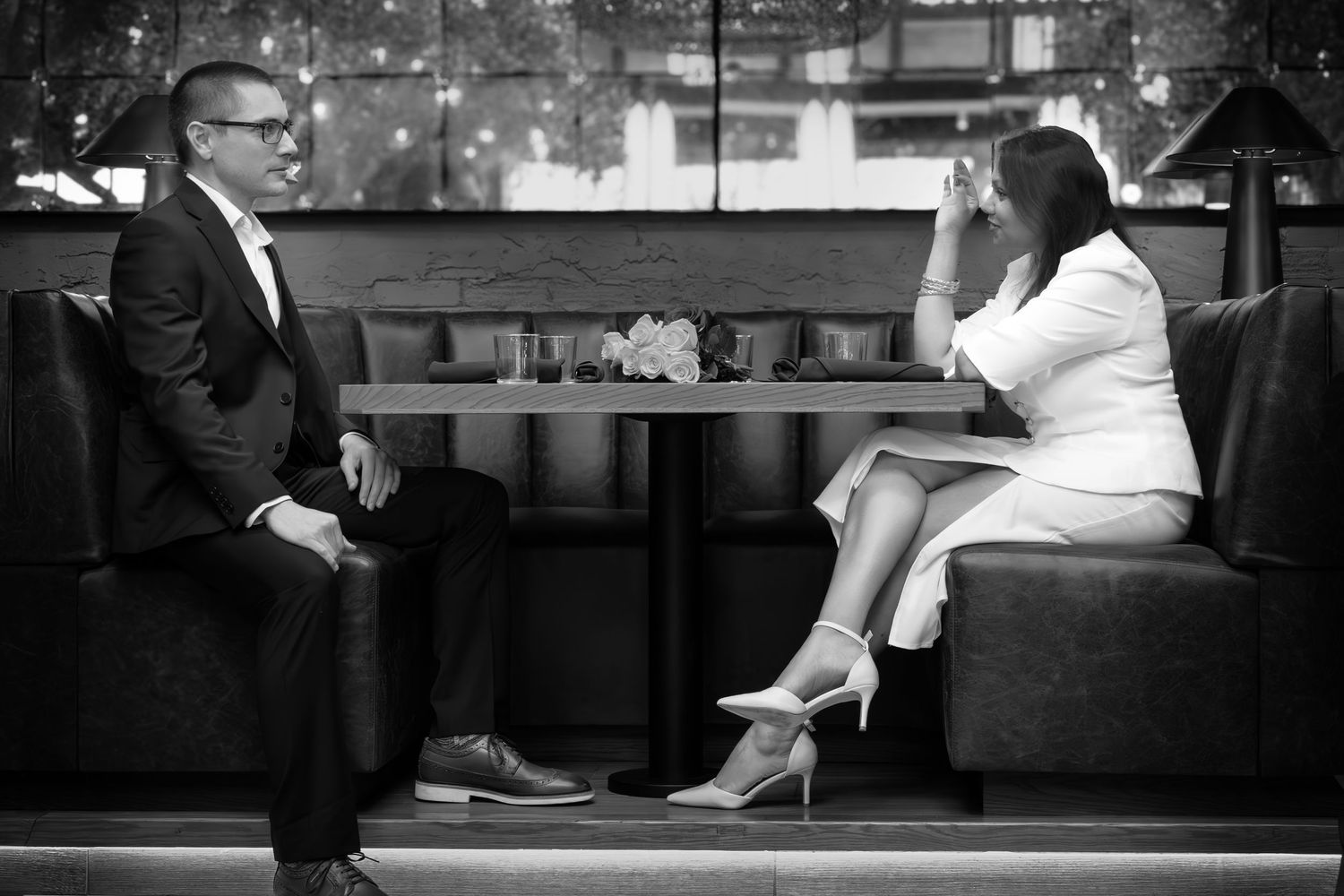 Black and white photo of a man and woman in formal attire having a conversation at a restaurant booth table.