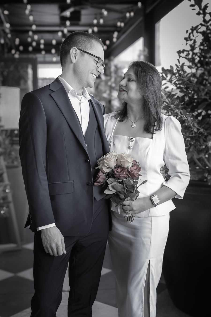 Black and white photo of a smiling couple in wedding attire, woman holding a bouquet of roses.