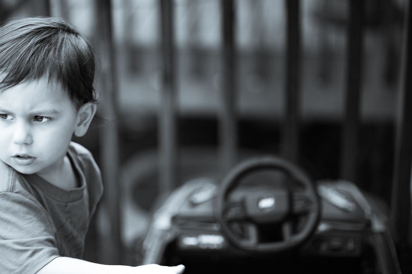Black and white photo of a young child leaning on a surface with a toy car in the background.
