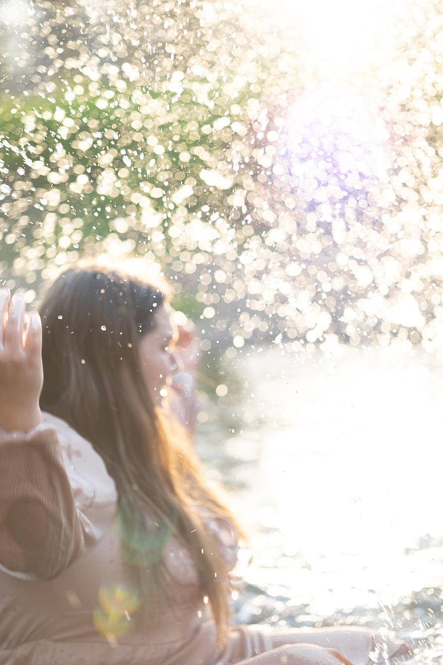 Dreamy sunlit portrait of a woman outdoors in water with bokeh light effects and golden lens flare.