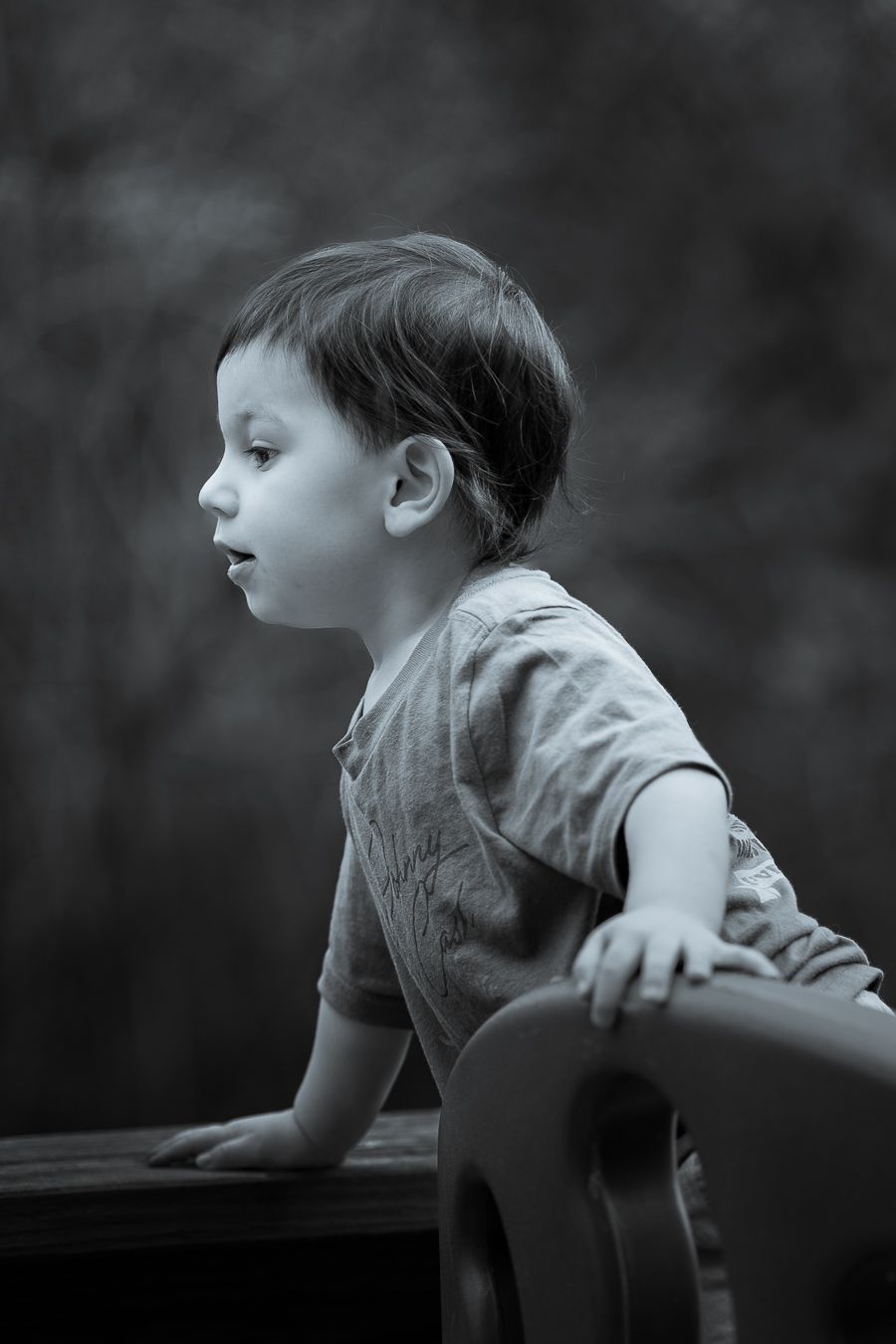 Black and white side profile of a young boy leaning on outdoor deck railing thoughtfully.