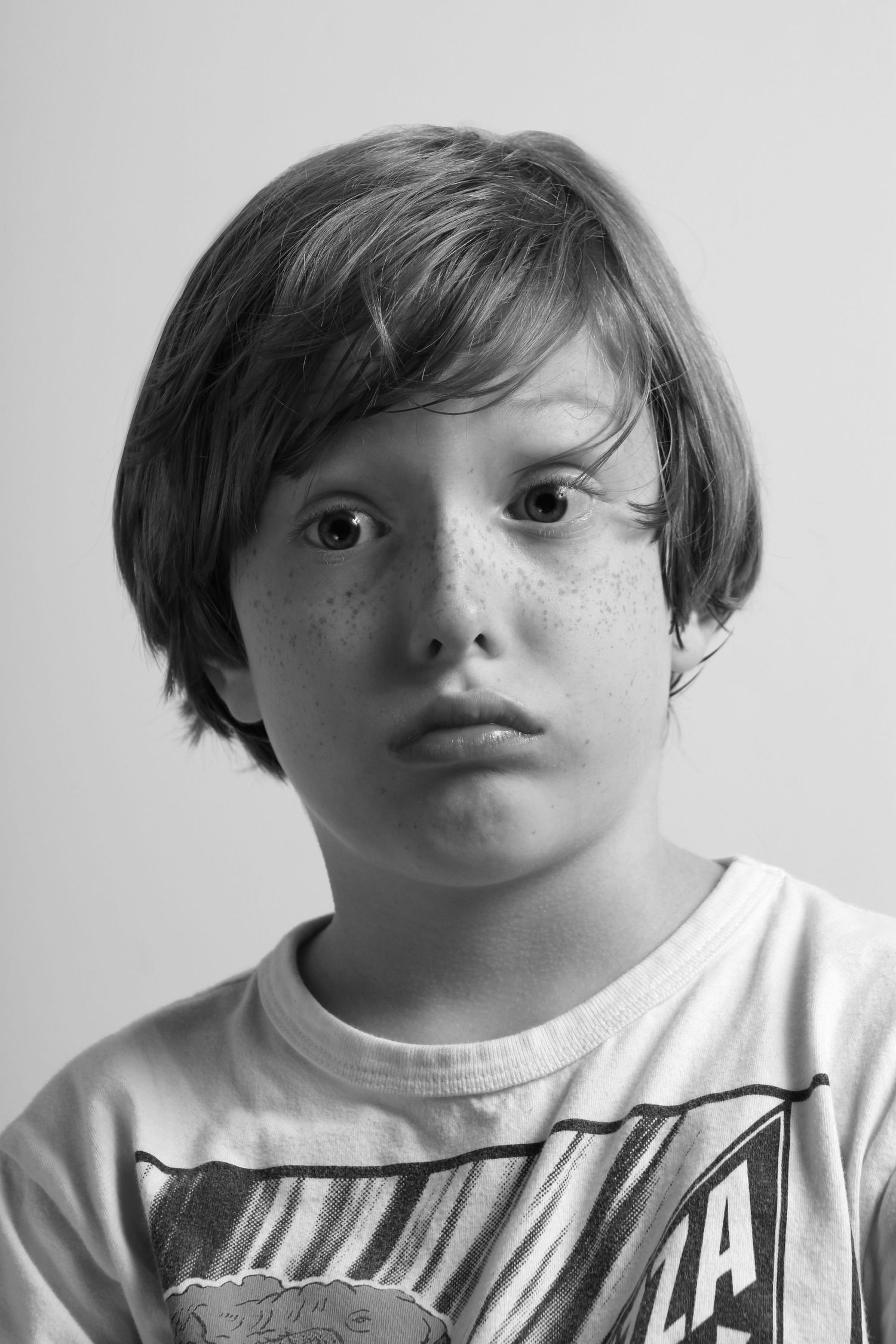 Black and white portrait of a freckled young boy with bowl cut hair wearing a graphic t-shirt.