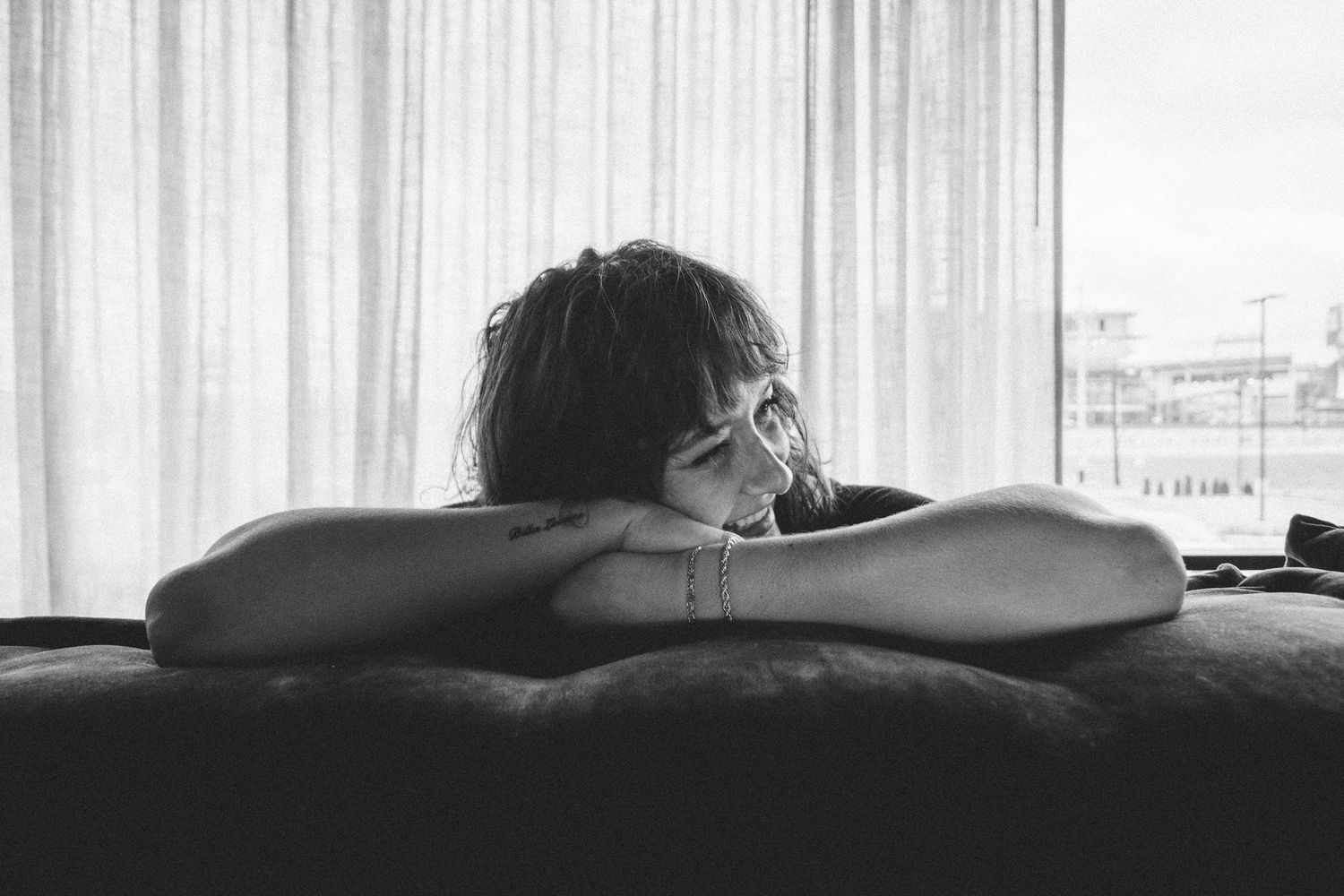 Black and white photo of a person resting their head on crossed arms on a dark couch.