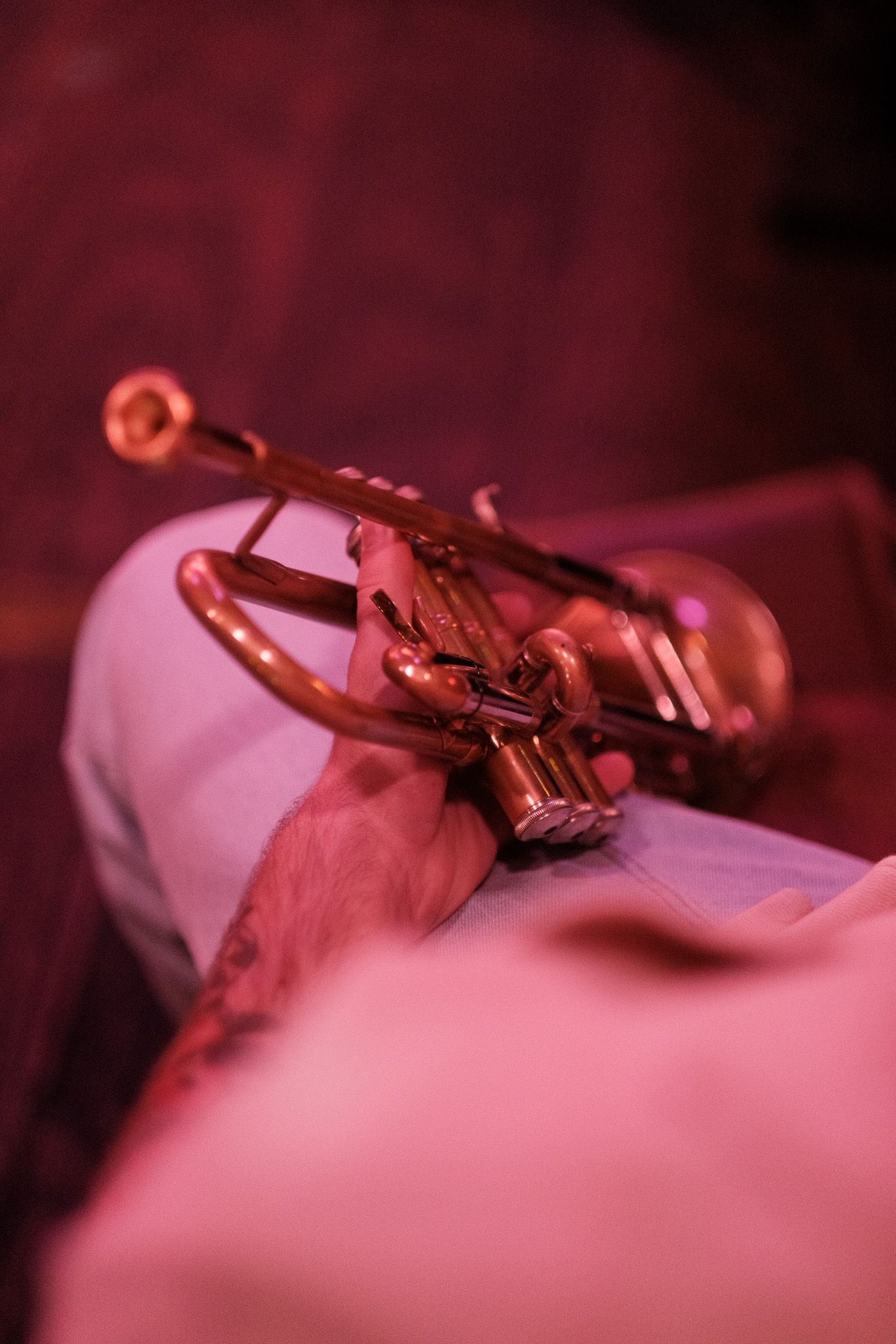 Close-up of a trumpet held in musician's hands under warm pink stage lighting.