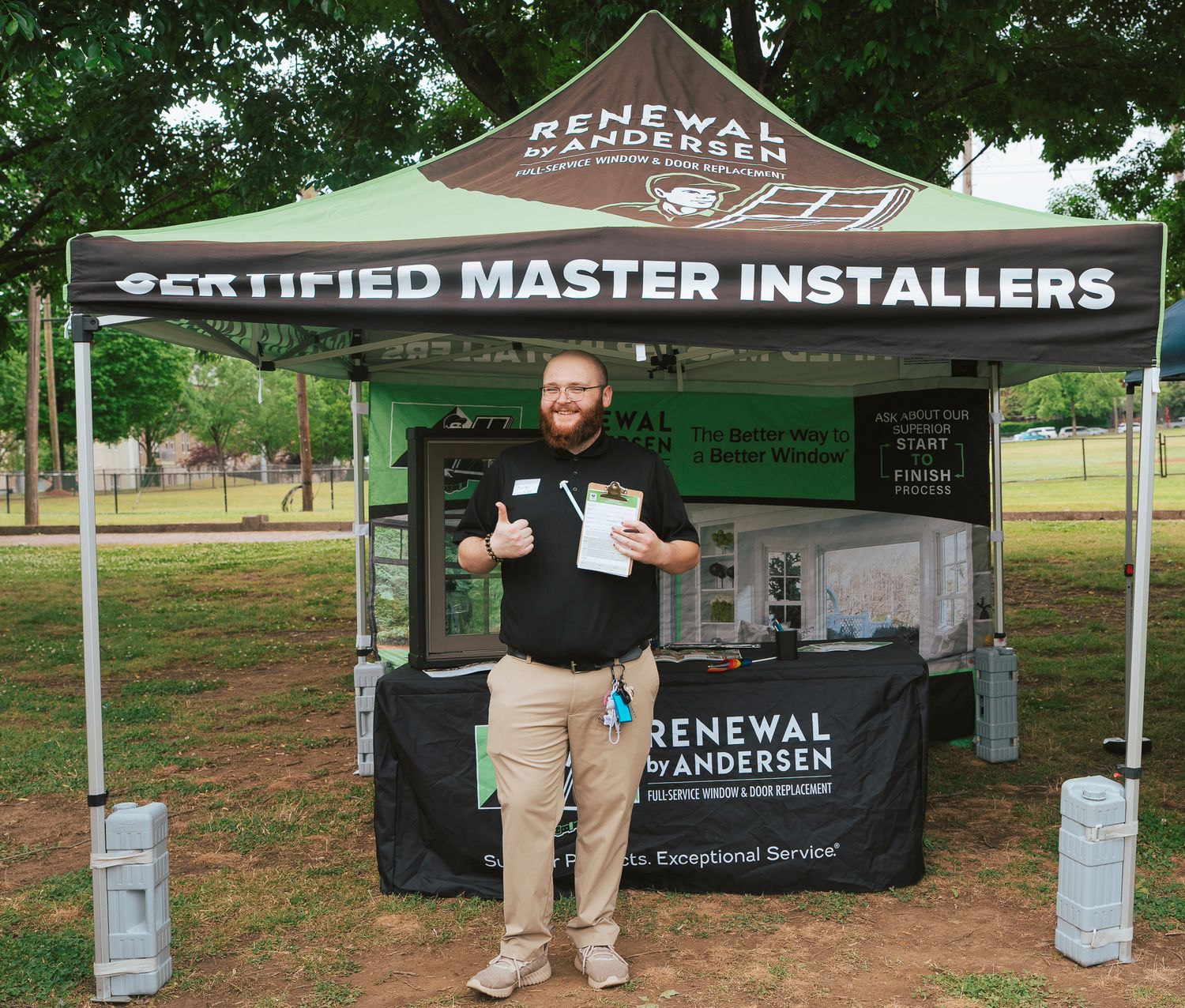 Man giving thumbs up at Renewal by Andersen Certified Master Installers booth at outdoor event.