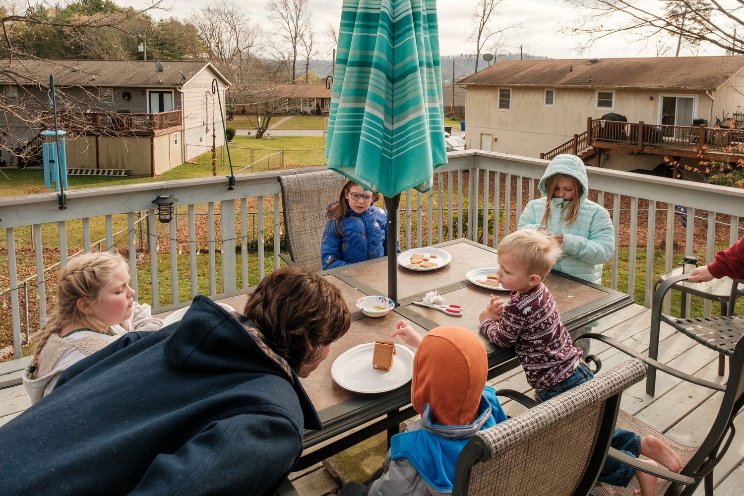 Family gathered around an outdoor patio table decorating gingerbread houses in fall.