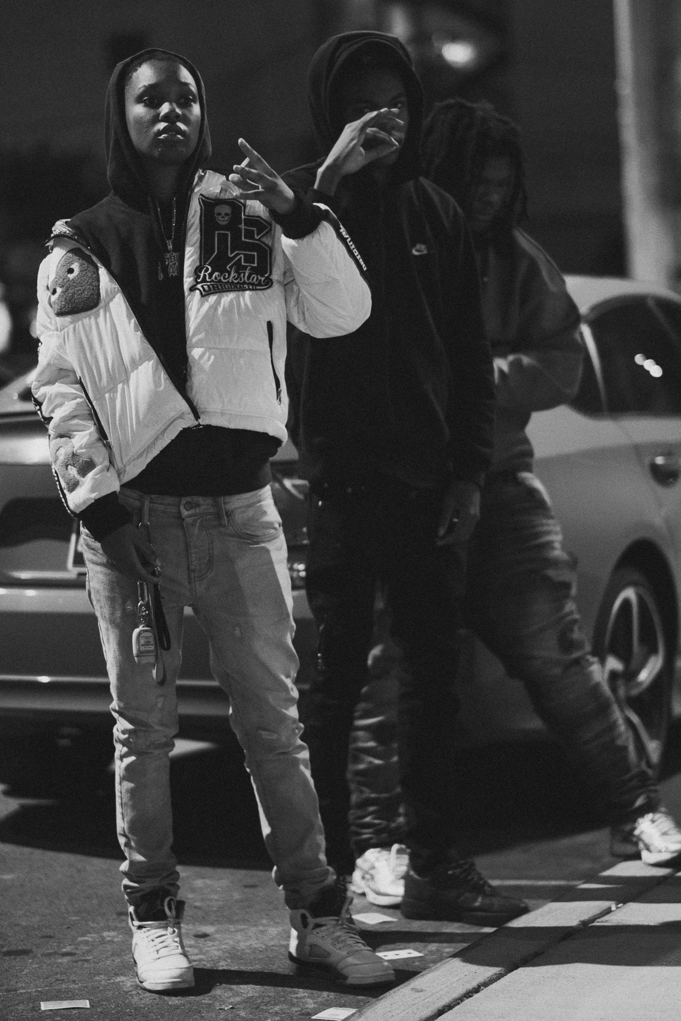 Black and white photo of two young men in hoodies posing on a street at night.