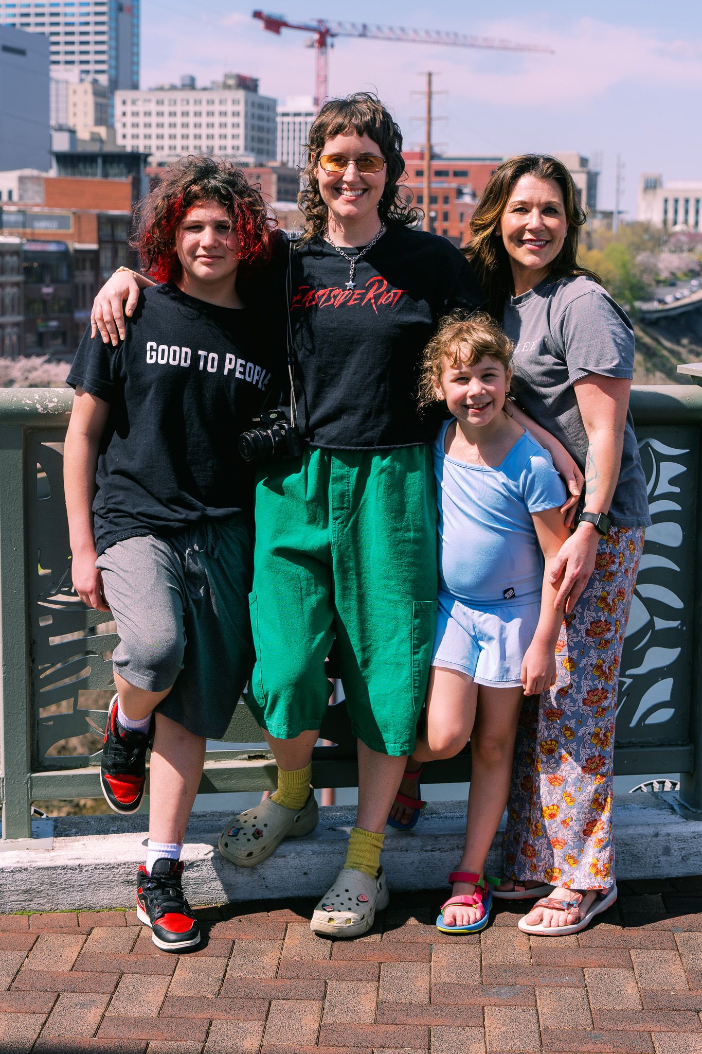 Family of four posing together on a bridge with a city skyline and construction crane in the background.