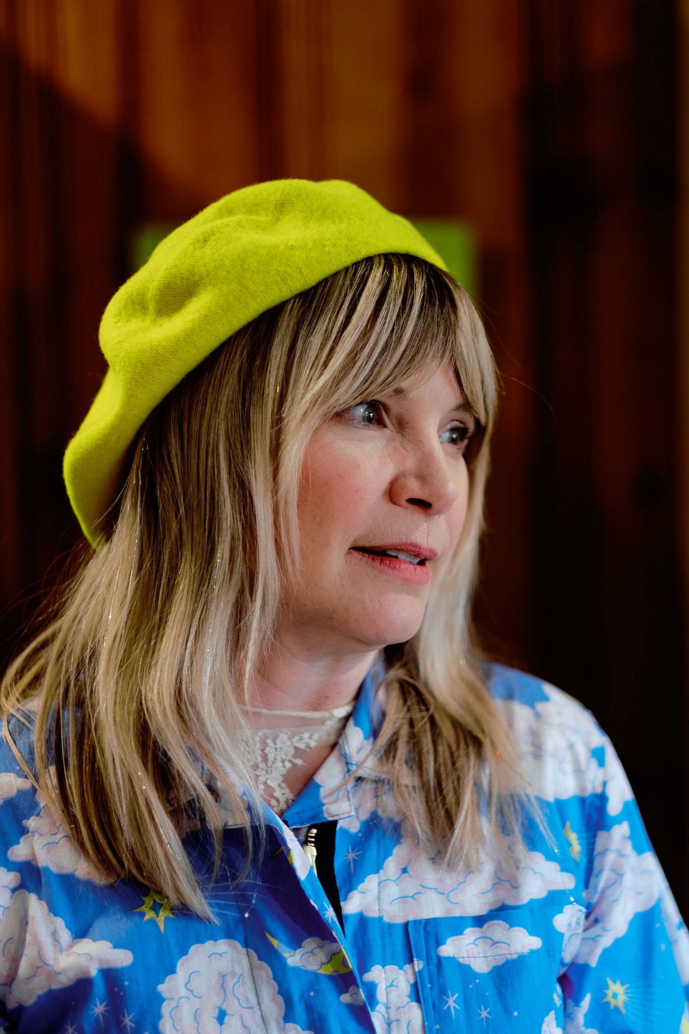 Older blonde woman wearing a bright yellow-green beret and blue floral jacket, looking to the side.