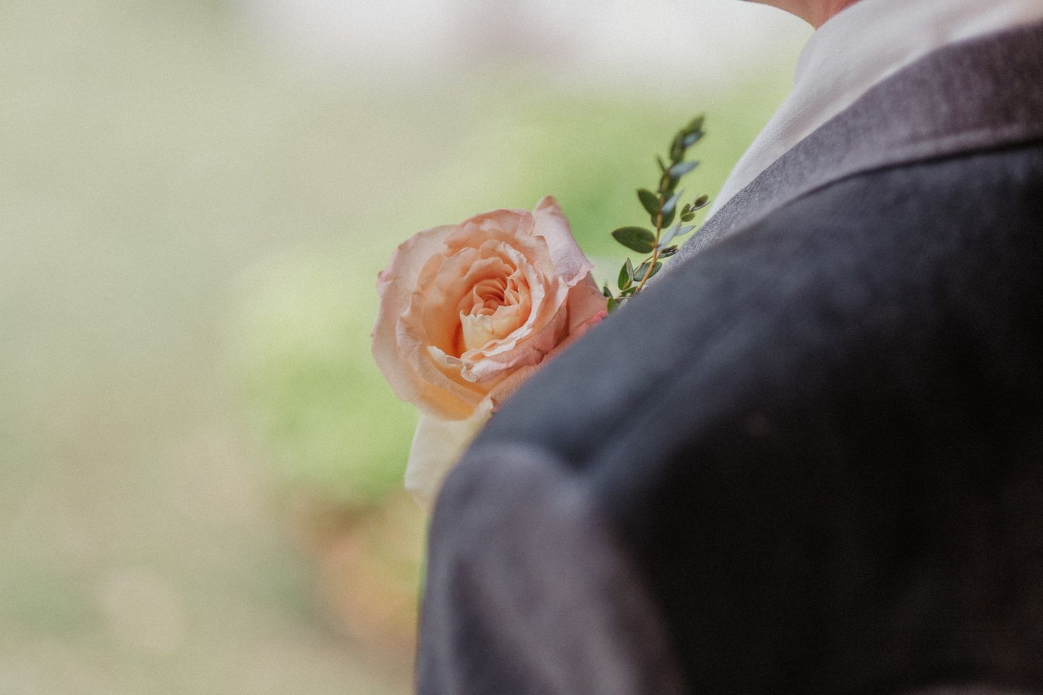 Close-up of a peach rose boutonniere pinned to a dark suit jacket lapel.