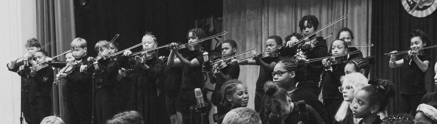 Black and white panoramic photo of young students playing brass instruments in a school concert performance.