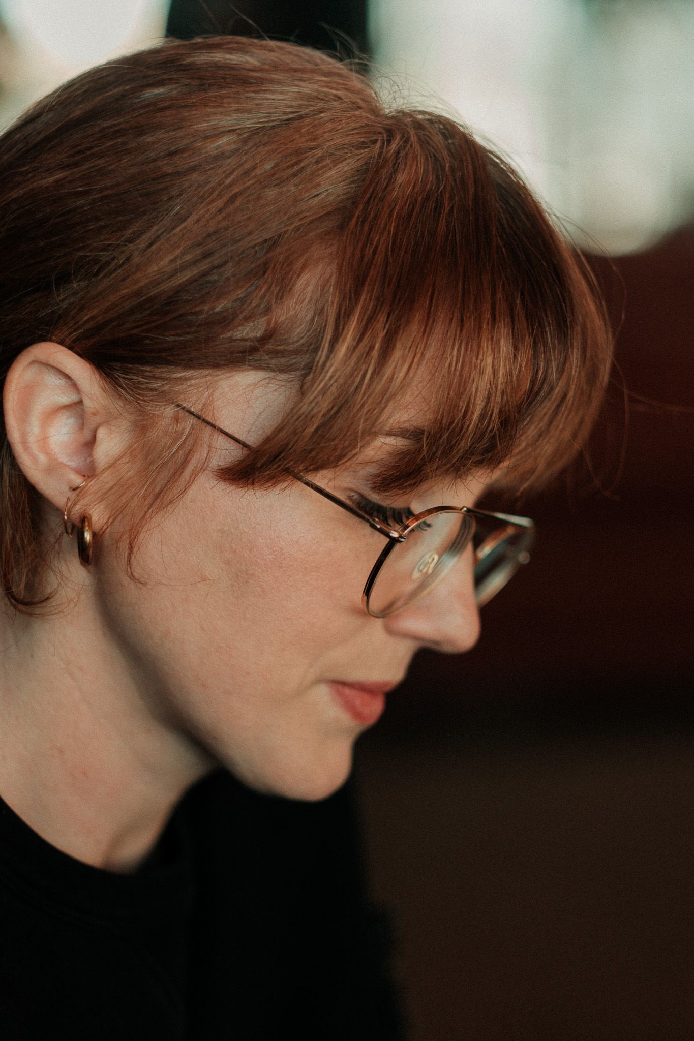 Side profile portrait of a young woman with auburn hair and round glasses looking downward.