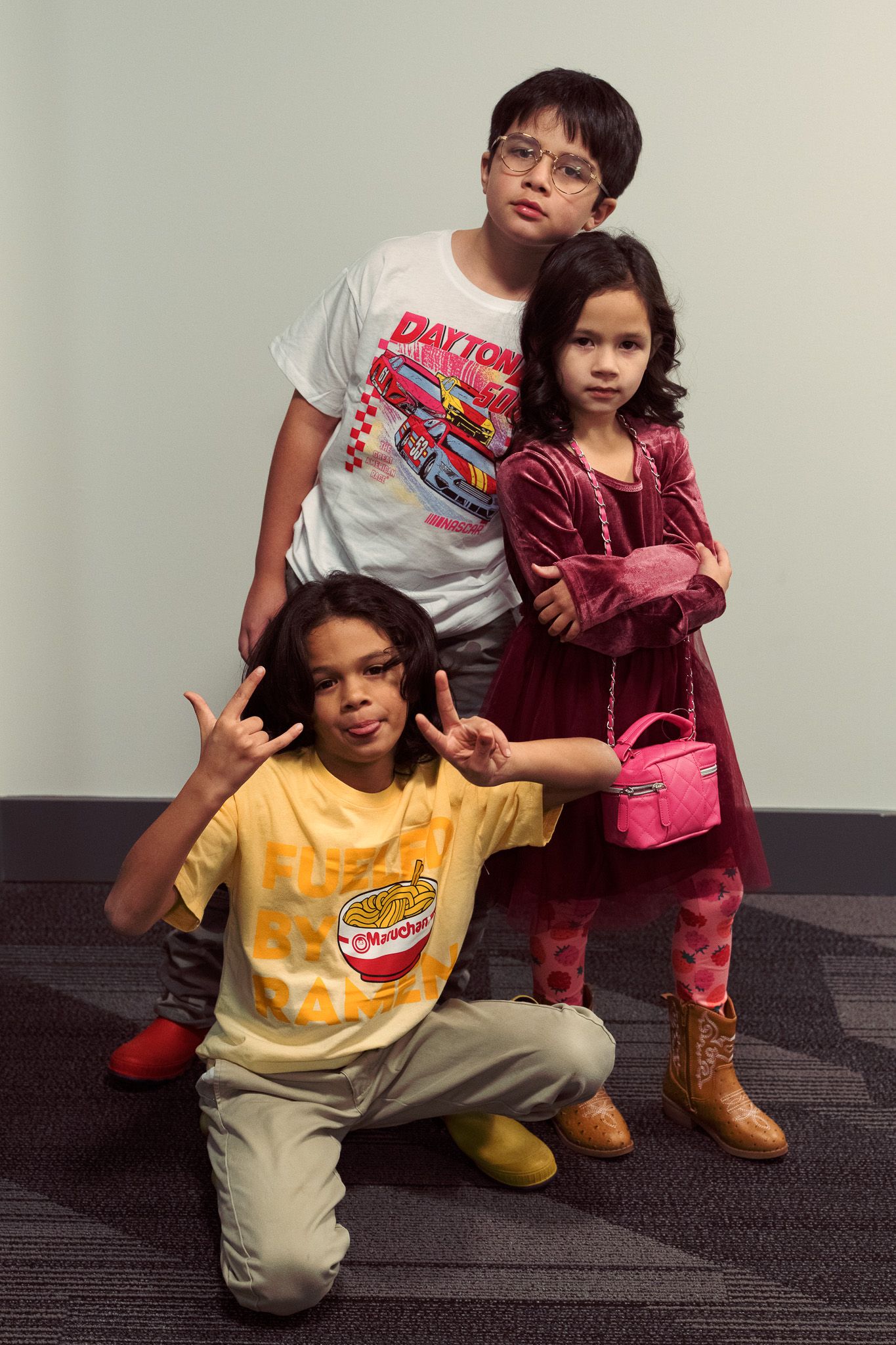 Three kids posing confidently, two standing and one crouching with peace signs.